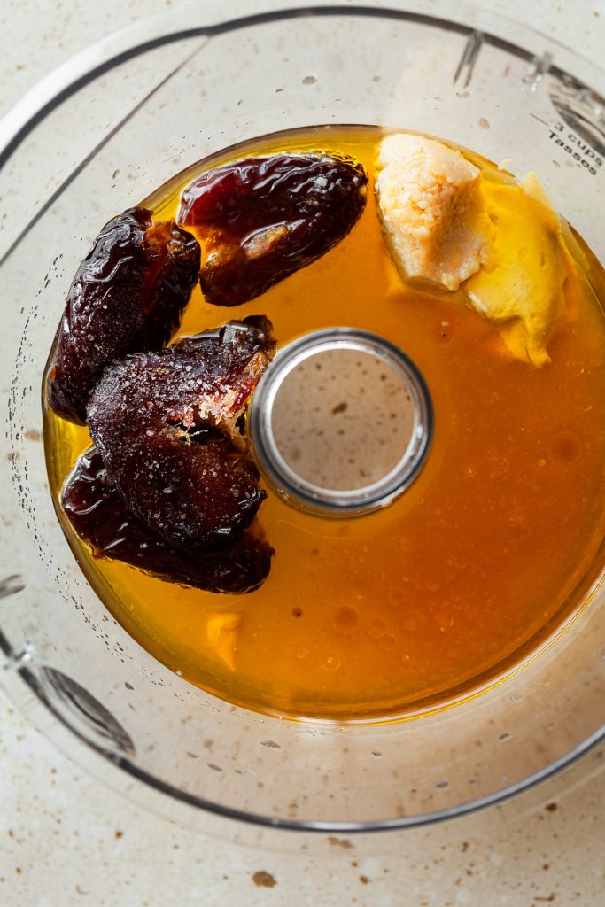 overhead view of date, mustard and vinegar in the bowl of a food processor.