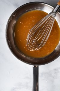 overhead view of caramel in a skillet with a whisk on a marble surface.