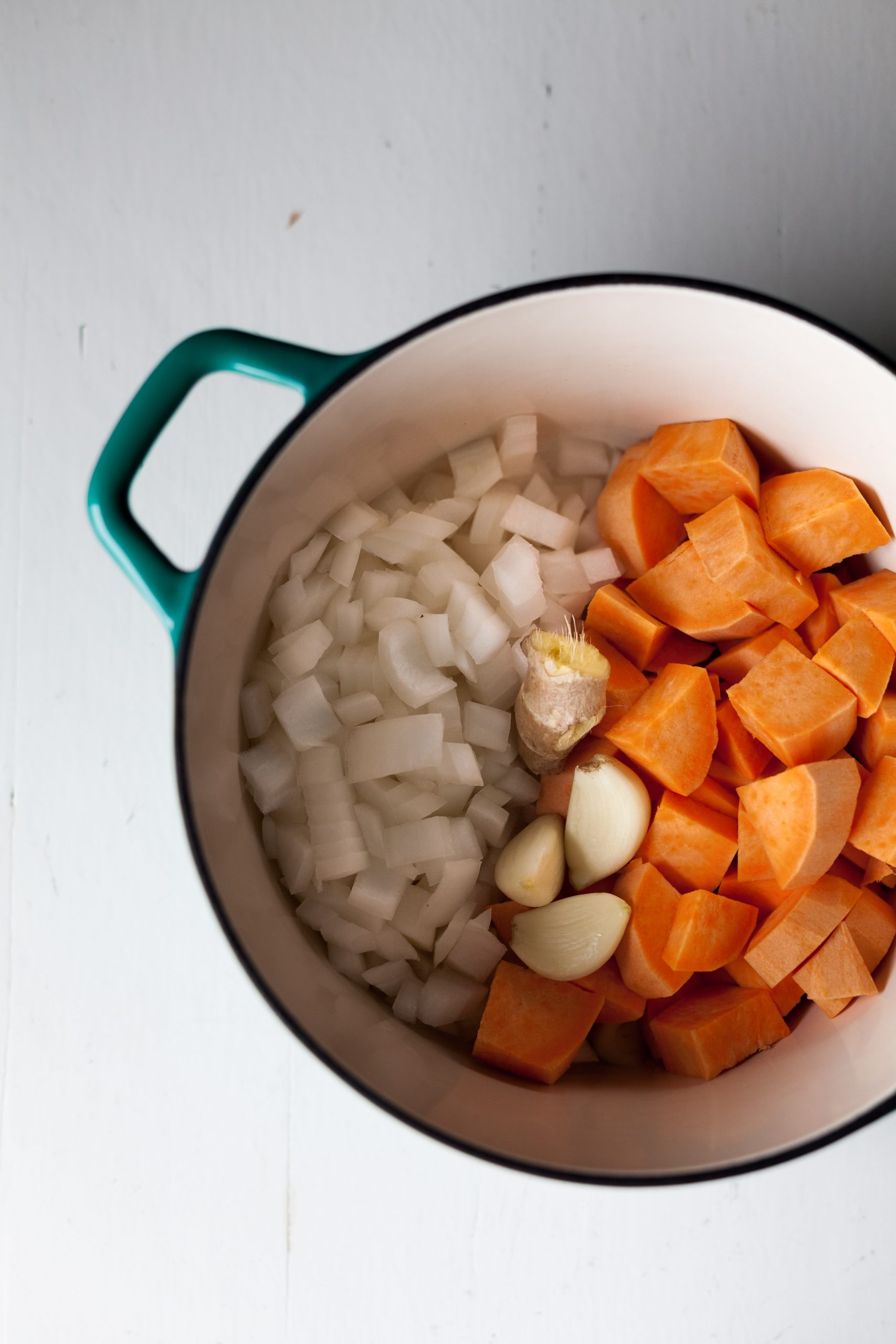 overhead view of a pot filled with diced onion, sweet potato and ginger on a white surface.