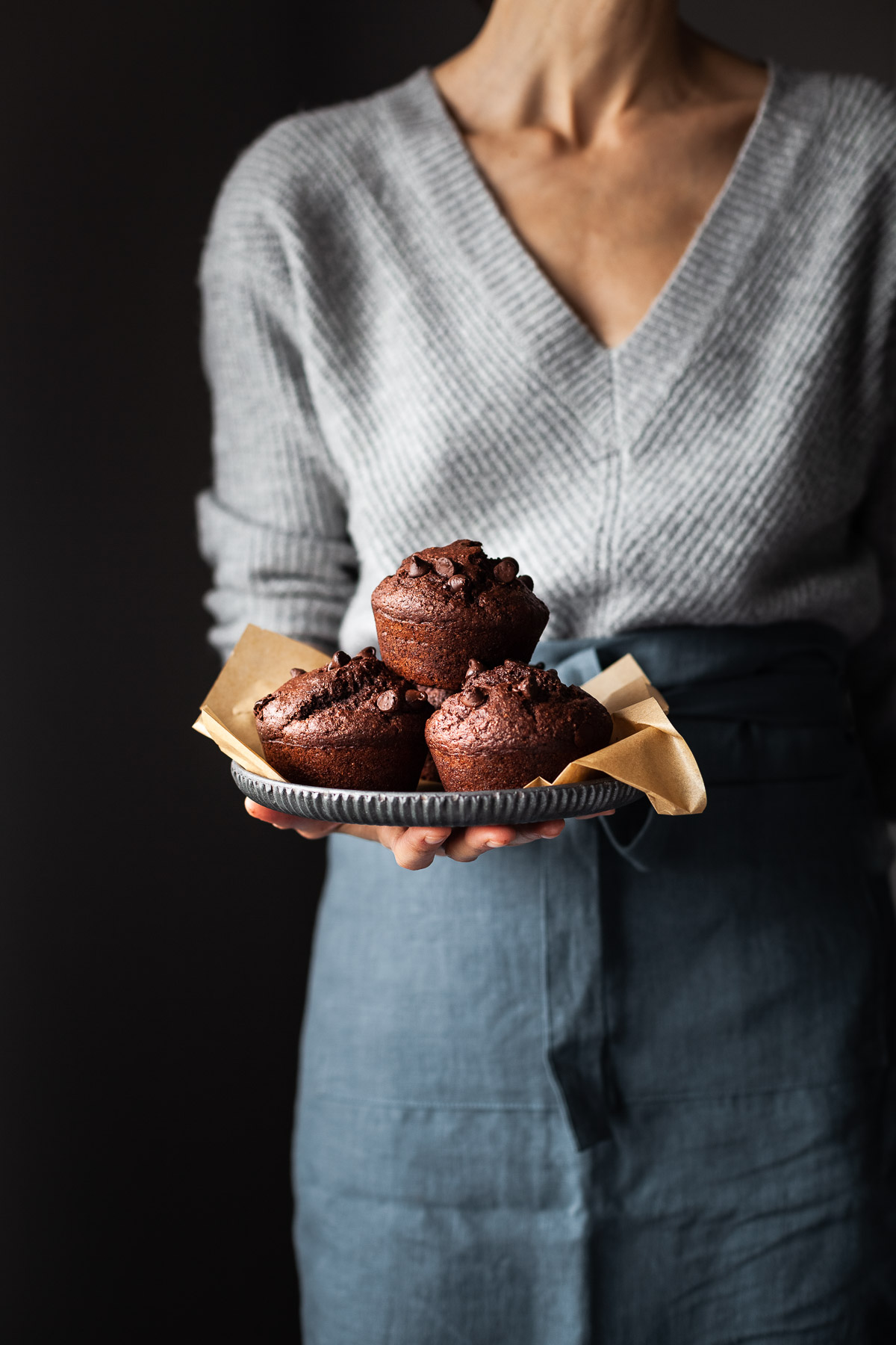 a baker in a grey sweater holding a tray with 3 chocolate beet muffins.