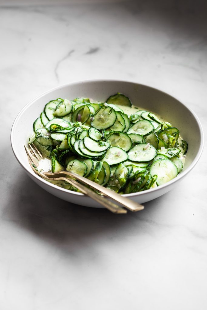 Side view of a large bowl of vegan German cucumber salad with gold serve ware.